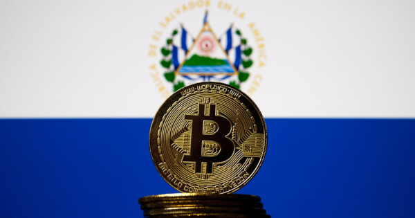 Bitcoin representation coin placed in front of blurred Salvador's national flag